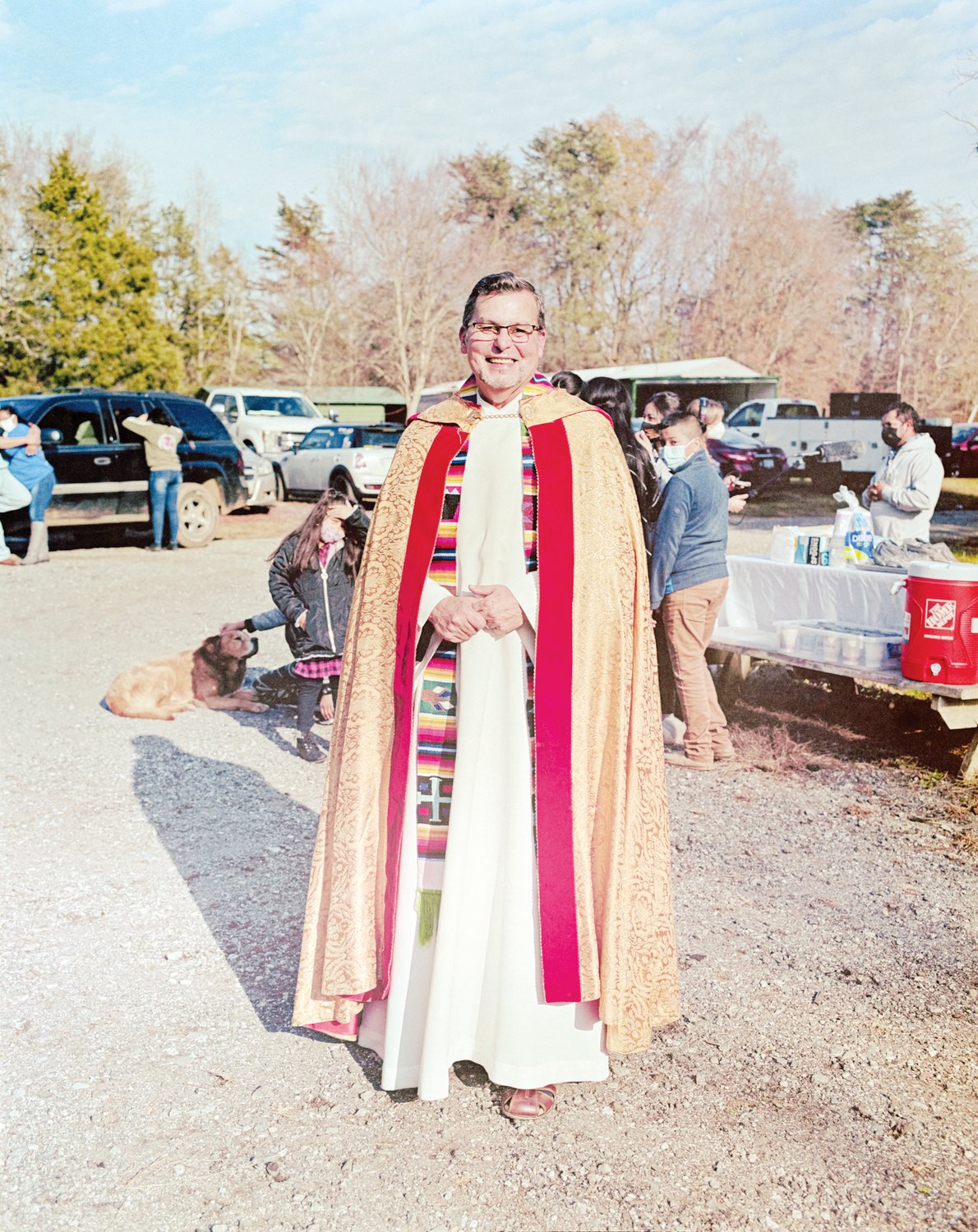 Father Julio Martinez of St. Julia Catholic Church in Siler City stands in his ceremonial robe and gown amid the busyness of food distribution post-blessing.
