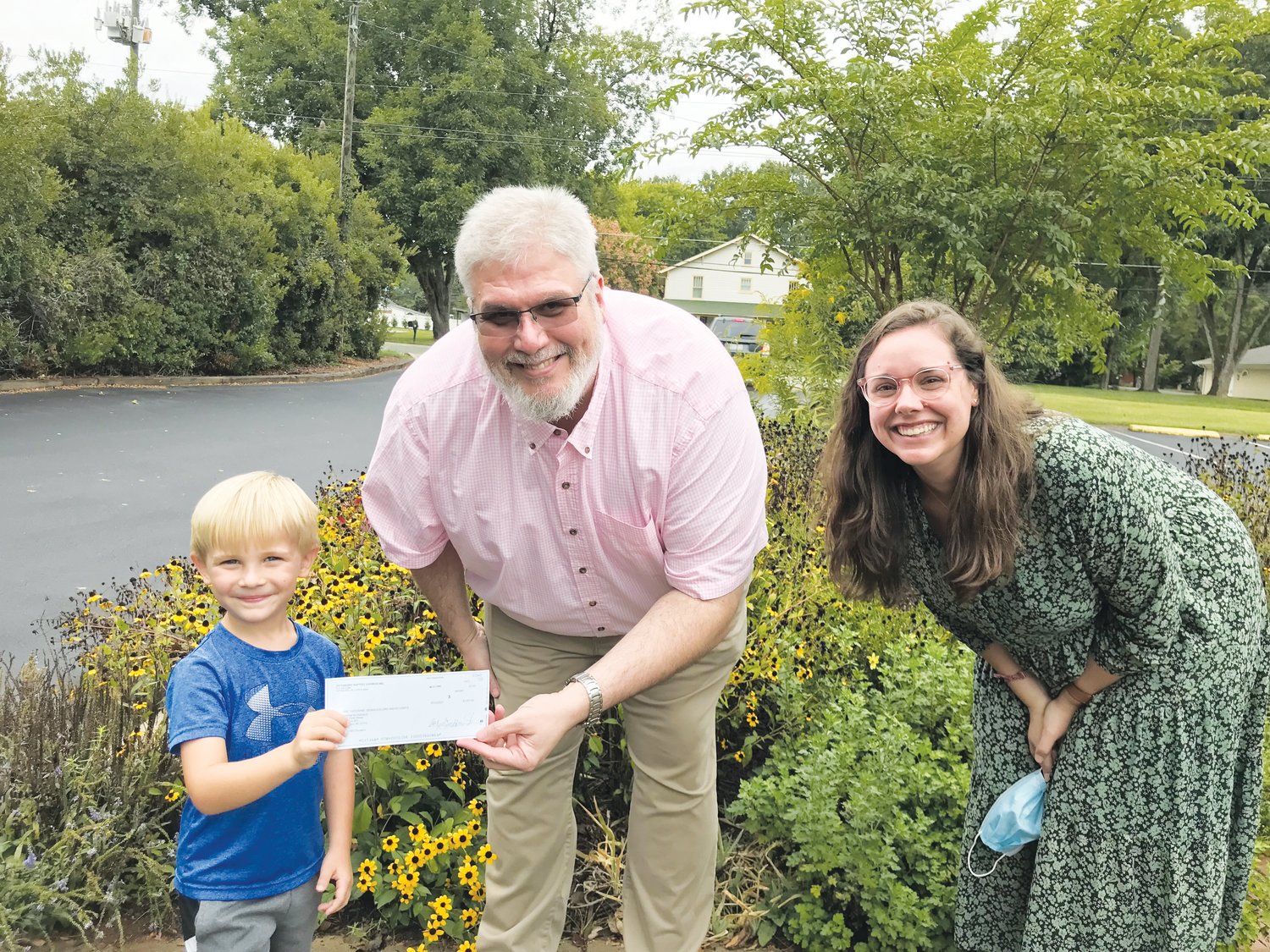 Carson Cashion, on behalf of participants of Pittsboro Baptist Church vacation Bible school, presents a check to Chatham Habitat for Humanity Business Manager Roderick Parker and Development Director Anna Spears..