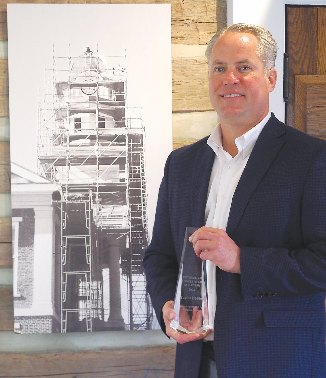 Hobbs poses with his recent award from the Chatham Chamber in front of a photo of the county's historic courthouse during its reconstruction.