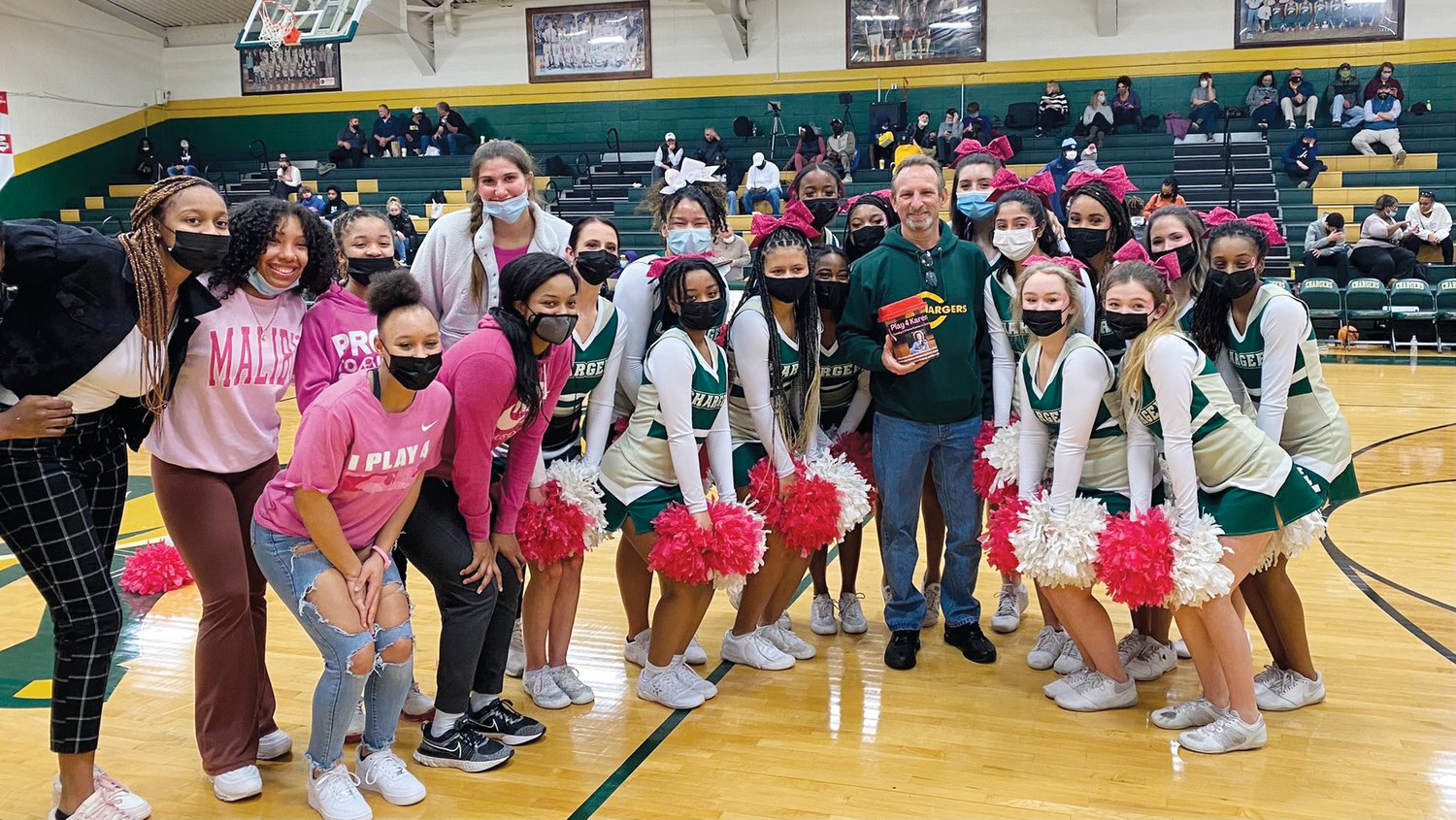 A group of Northwood women's basketball players and cheerleaders poses alongside Thomas “Newt” Heilman II (center, green hoodie), the husband of late educator and coach Karen Sbrollini Heilman, who was honored with the 'Play4Karen' fundraiser during the Chargers' annual 'Pink Night,' which raised over $500 for a scholarship in her name.