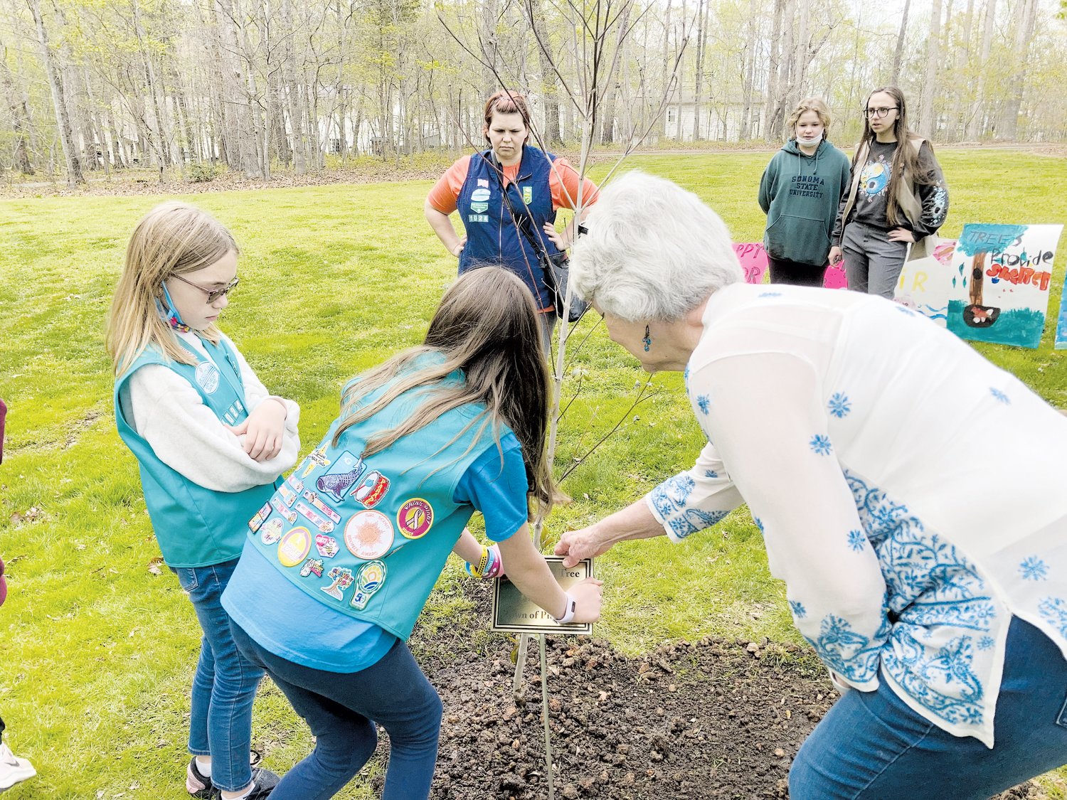 Mayor Cindy Perry helps two Girl Scount Juniors place a plaque for this year's Arbor Day tree.