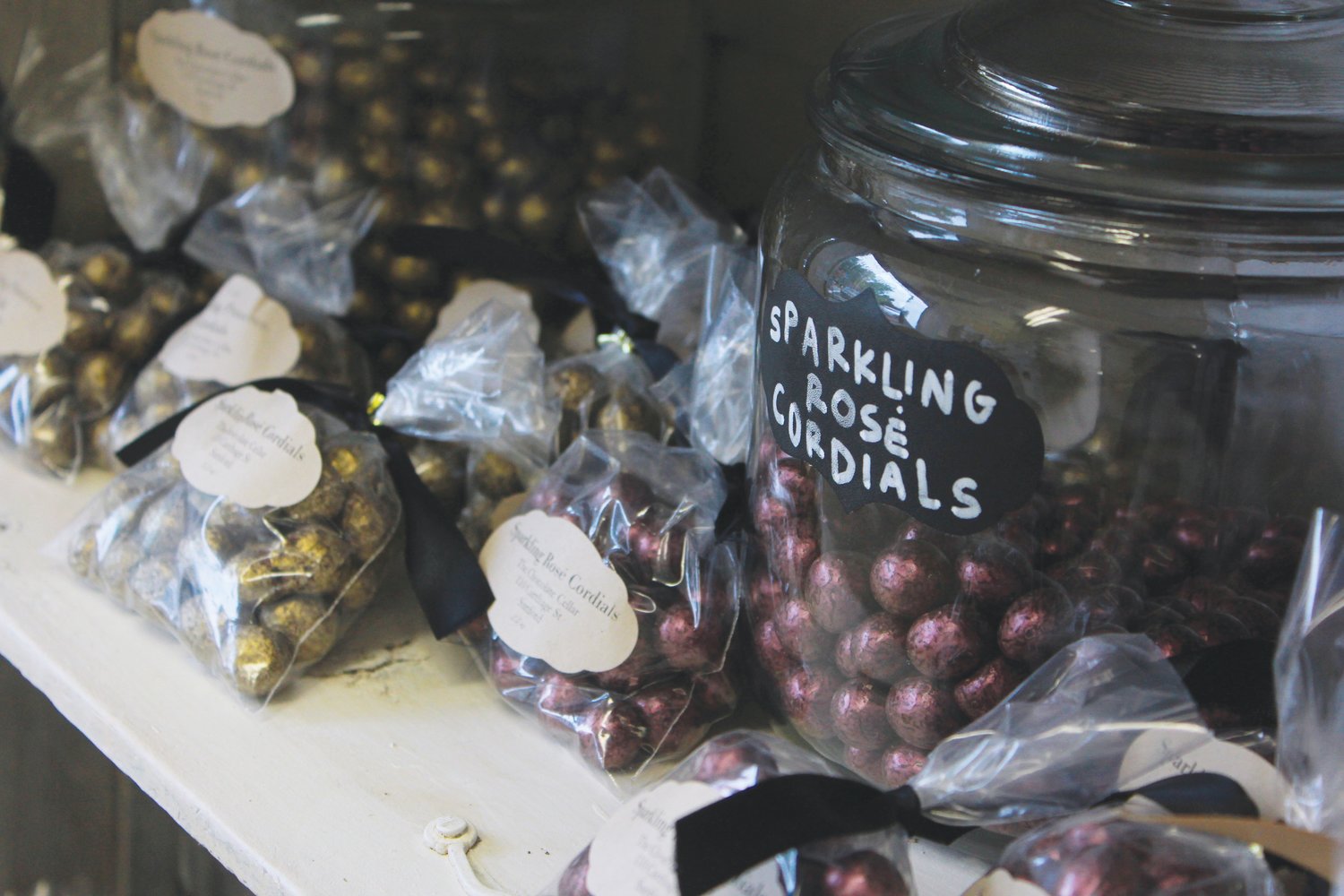 Sparkling rose cordials fill up glass jars and bags on a shelf inside the Chocolate Cellar Deux in Pittsboro.