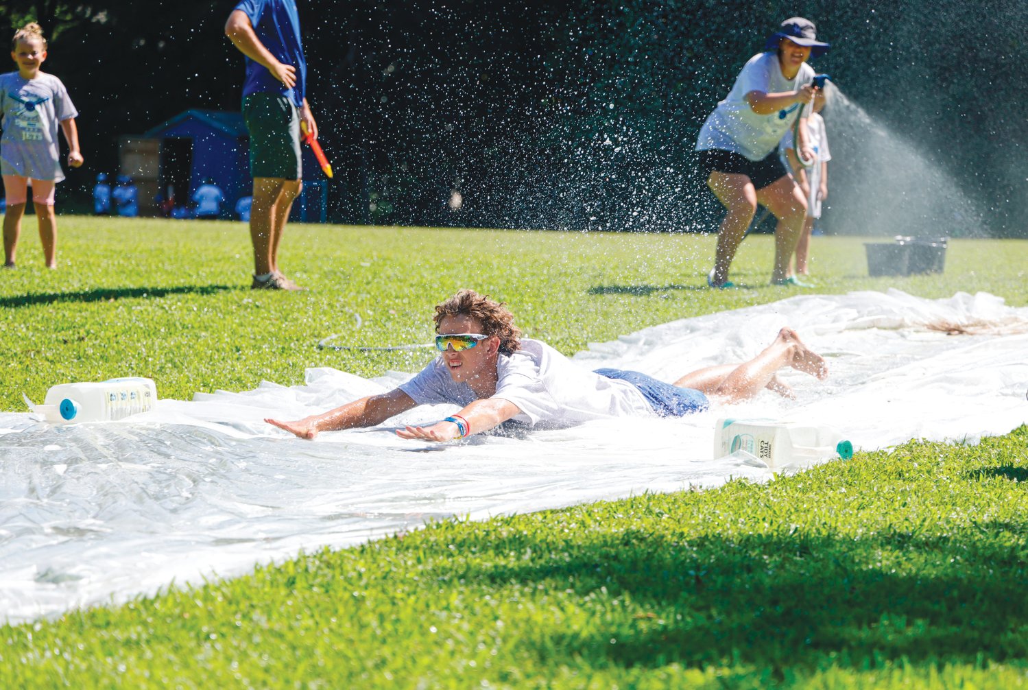 Jordan-Matthews junior Kelton Fuquay (center) takes a break from the heat by sliding down a slip 'n slide on the final day of the Jets' annual baseball camp last Thursday as J-M softball head coach Holly Clark (right) provides the water.