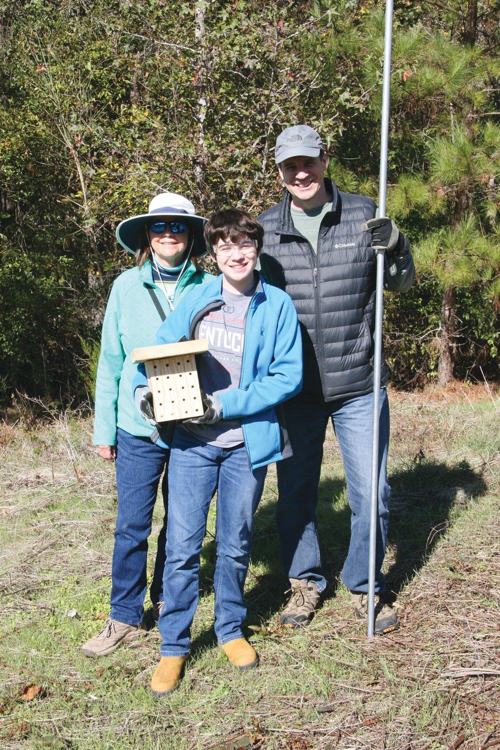 Gretchen Smith stands with Boy Scout Ben Pickens and his father Dr. Ed Pickens installing a bee house in the pollinator meadow created for Friends of Lower Haw as part of an Eagle Scout project.